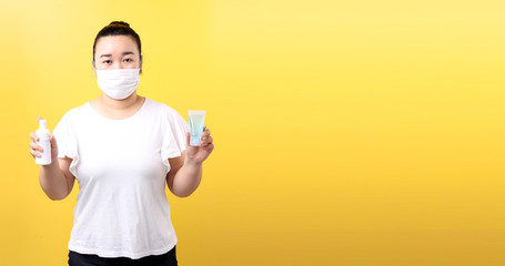 Fototapeta na wymiar Asian woman using alcohol gel and wearing medical mask,Recommend the prevention of viruses and various diseases. isolated on yellow background in studio With copy space.