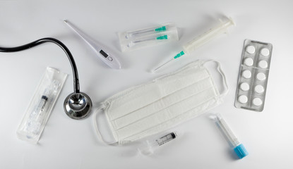 Fototapeta premium Medical equipment isolated on white background. Surgical protection face mask, syringes, needles, test tube, digital thermometer, pills and stethoscope. Corona Covid-19 protection concept, top view.