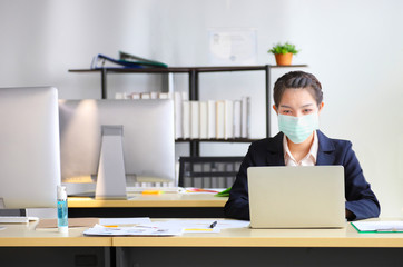 Female employee wearing medical face mask while working alone because of new normal social...
