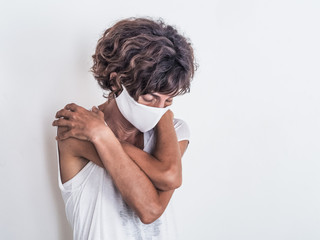 lonely worried depressed woman wearing a white medical face mask from virus covid-19 and hugging herself while looking down with closed eyes full of fear and lonliness because of social distancing