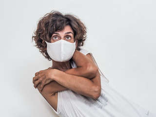 lonely and sad woman wearing a white medical face mask protecting from corona virus covid-19 and hugging and loving herself in fear because of social distancing