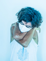 lonely and sad woman wearing a white medical face mask protecting from corona virus covid-19 and hugging and loving herself in fear because of social distancing