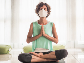 meditating woman wearing a medical face mask to protect from corona virus covid-19 in crossed...