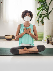 meditating woman wearing a medical face mask to protect from corona virus covid-19 eyes closed in...