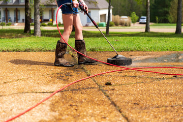 Woman pressure washing to clean driveway of a home