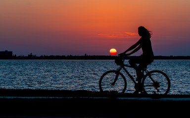 Fototapeta na wymiar Silhouette of a woman on a bicycle. A girl ride on the bicycle. Beautiful ocean sunset. Sport and recreation. Copy space.