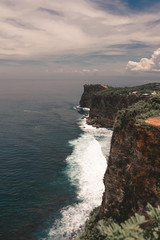 Beautiful girl with long hair on a huge rock overlooking the ocean. Cliff with the waves of the Indian Ocean in Bali. Indonesia. Travels