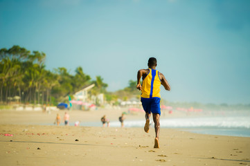 rear view of young athletic and fit african american sport man doing running workout on sunset at the beach training hard jogging barefoot on sand in healthy lifestyle