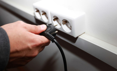 male hand sticks a plug into a socket