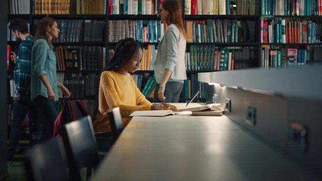 University Library: Gifted Black Girl uses Laptop, Writes Notes for the Paper, Essay, Study for Class Assignment. Students Learning, Studying for Exams College. Side View Portrait with Bookshelves