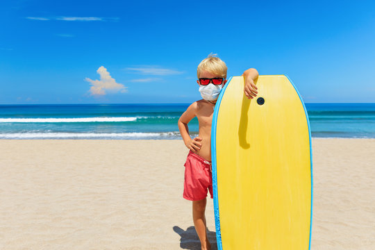 Young Surfer Wearing Sunglasses, Protective Mask On Sea Beach With Body Board. Summer Tours, Cruises Cancellation Due To Coronavirus COVID-19 Epidemic. Safe Travel Destinations For Family Vacation.