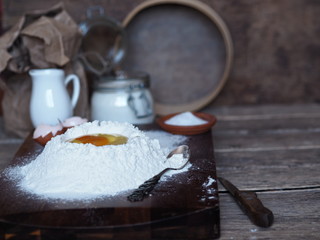 Pastry concept.On the kitchen cutting Board, a broken egg in flour with ingredients for making dough and kitchenware. Home cooking.