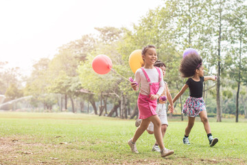 happy children playing with colorful toy balloons outdoors. Kid having fun in green spring field against blue sky background. happy multi-ethnic children playing. freedom and imagination concept.