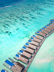 The drone photo with a wooden water villas seen from above and an amazing blue lagoon crystal clear water close to tropical lagoon. Amazing summer travel and vacation background. Dreamy beach scenery