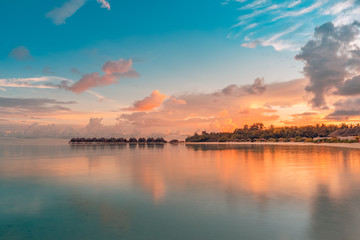Sunset on Maldives island, luxury water bungalow resort and paradise island silhouette. Beautiful sky and clouds and beach background for summer vacation holiday and travel concept