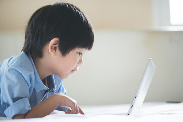 Asian boy lying in bed and using laptop