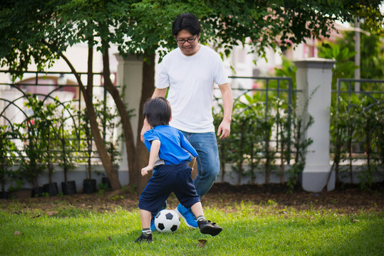 Asian father Father and son playing football in the garden