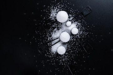 Black measuring spoons with salt on black background.