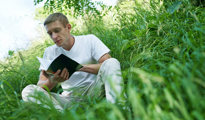 Naklejka na ściany i meble man sitting in the quiet green grass and reading a book