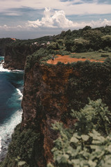 Beautiful girl traveler with long hair and a slender body stands on a cliff of a cliff overlooking the waves of the blue ocean.Bali Island, Indonesia. Travel and tourism concept in exotic and tropical