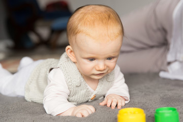 Focused cute red haired baby girl playing learning game with toys. Six month child crawling on grey carpet on floor. Childhood or baby care concept