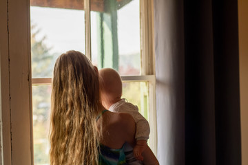 Stay home: a blond girl holds her baby brother near the window. Self isolation coronavirus concept