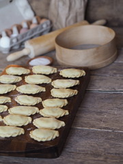 Cooking homemade dumplings.In the kitchen, there is a cutting Board, ready-made dumplings with ingredients for making dough and kitchen utensils.Ancient wooden background.