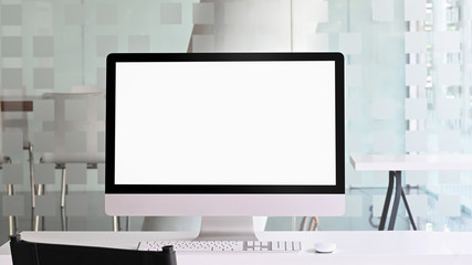Photo of computer monitor with white blank screen putting on white working desk with wireless mouse and keyboard over orderly office as background.