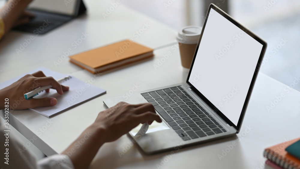 Poster Cropped image of secretary woman's hands typing on computer laptop with white blank screen that putting on orderly working desk that surrounded with notes, coffee cup and stack of books.
