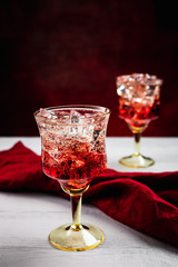 Two beautiful refreshing sparkling cocktails with ice, white wooden table, dark background with red tint, red napkin