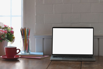 Computer laptop, ceramic coffee cup, notebook, notes and bunch of flowers putting together on wooden working desk over brick wall as background.