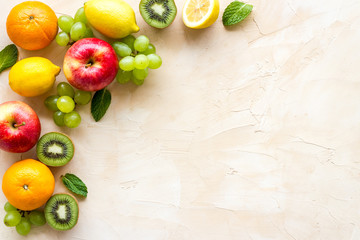 Fresh fruits background with citruses, apple, kiwi and grape on beige table top-down frame copy space