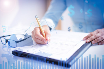 Businesswoman making notes with financial analysis graphs. Entrepreneur sitting at desk and writing. Paperwork concept. Cropped view.
