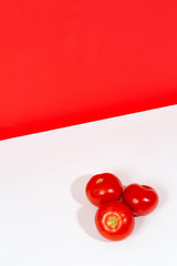 Three red tomatoes in a pile on white surface with red color block background