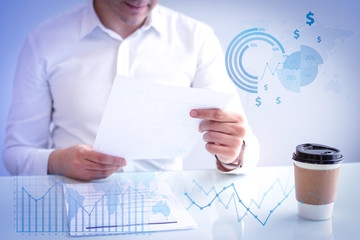 Smiling man looking at document with financial analysis graphs. Caucasian HR manager sitting at table with coffee cup and reading candidate resume. Employment concept