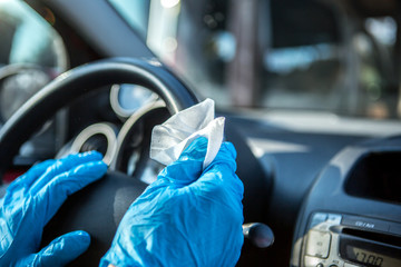 Coronavirus Epidemic Outbreak. Close-up of hand in protective glove using wet wipe to disinfect car steering wheel.  - obrazy, fototapety, plakaty