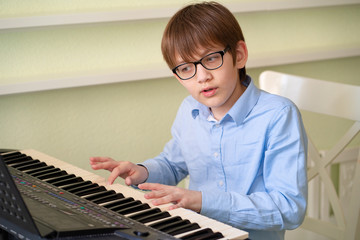 boy with glasses learns to play the synthesizer.