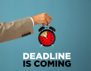 Businessman holding alarm clock and text DEADLINE IS COMING on color background