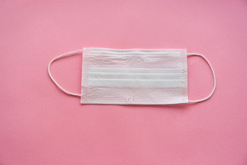 a disposable medical mask on a pink background.