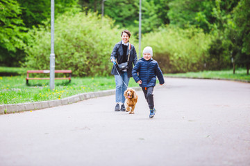 young woman with little kid and dog on leash walking at city park