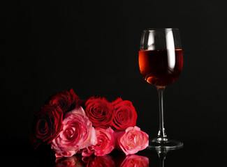 Glass of wine with rose flowers on dark background
