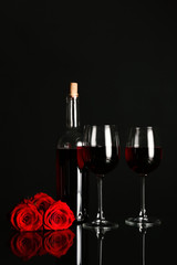 Glasses and bottle of wine with rose flowers on dark background