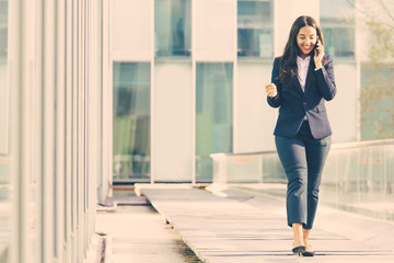 Smiling Asian businesswoman talking on smartphone. Full length portrait of cheerful office worker communicating through phone. Technology concept
