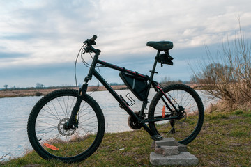 View of the lake and sky with sunset from behind a black sports mountain bike