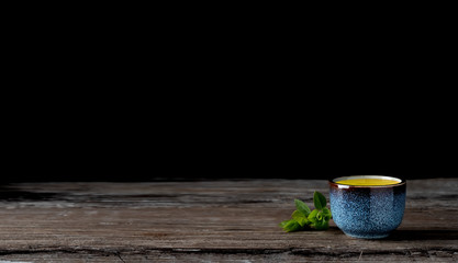 Bowl with matcha green tea on a vintage wooden table, dark background. Tea leaves next to the cup....