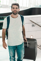 Smiling young man walking with luggage. Cheerful handsome Hispanic traveler strolling at airport. Travel concept