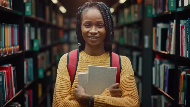 University Library Study: Portrait of a Smart Beautiful Black Girl Holding Study Text Books Smiling Looking at the Camera. Authentic Student Does Research for Class Assignment, Exams Preparationtion