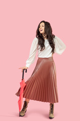 Young pretty dark-haired woman in a pleated skirt holding a red umbrella