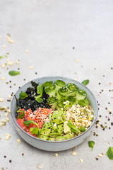 Salted salmon poke bowl with avocado, sea cale, cucumber, sesame seeds and bean sprouts on grey background