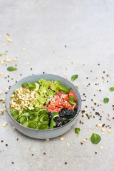 Salted salmon poke bowl with avocado, sea cale, cucumber, sesame seeds and bean sprouts on grey background